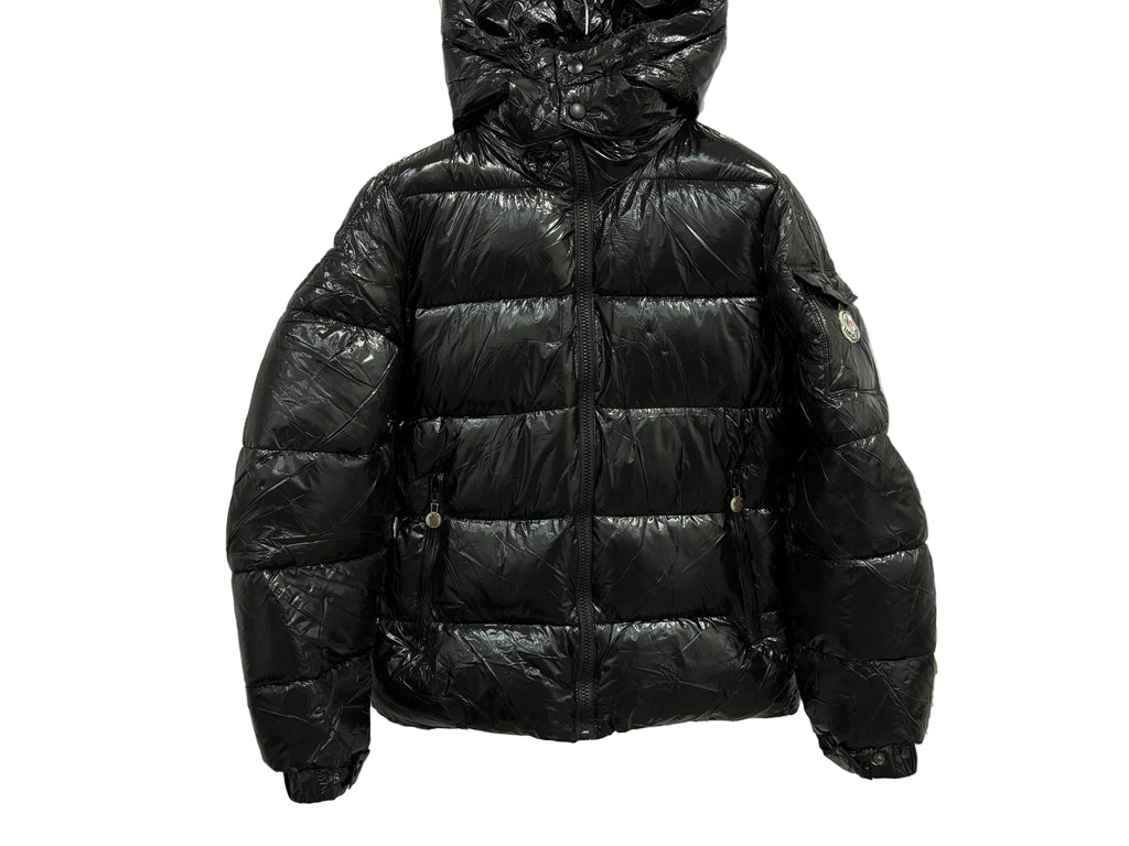 GIUBBINO MONCLER in glossy black on a marble background, showcasing its stylish design and warm insulation.