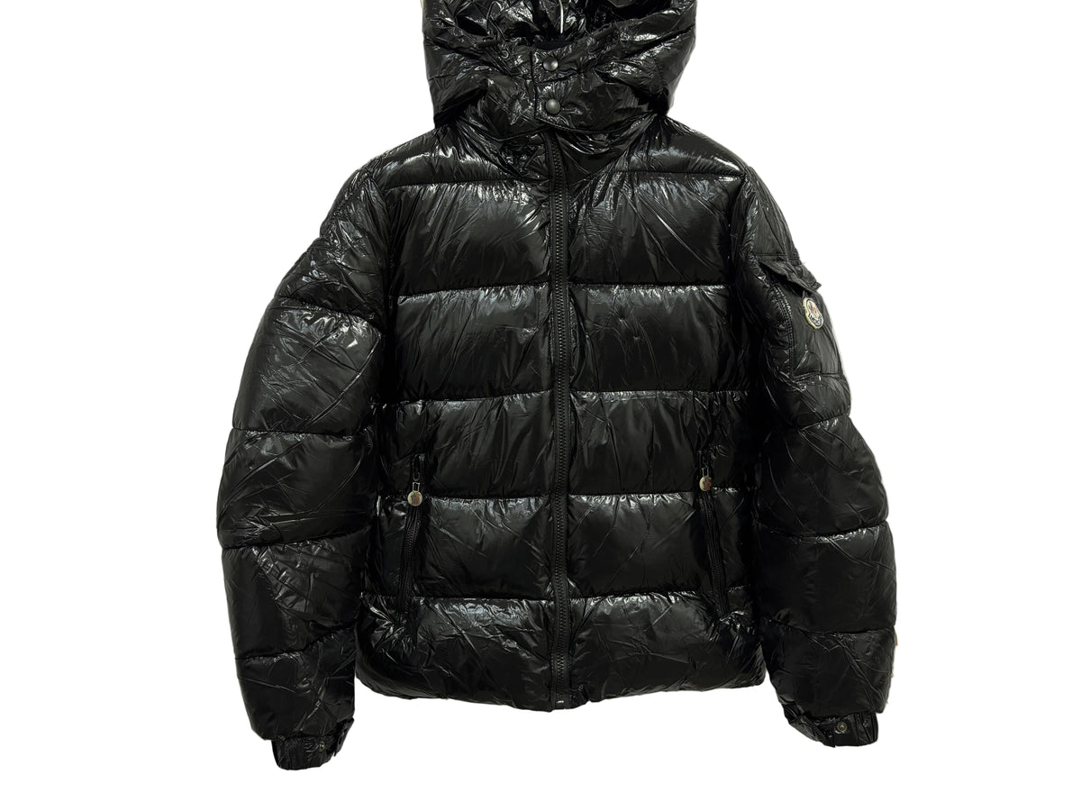 GIUBBINO MONCLER in glossy black on a marble background, showcasing its stylish design and warm insulation.