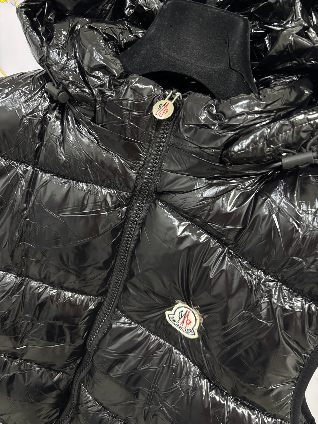 Close-up of SMANICATO MONCLER jacket with shiny black fabric and logo detail.