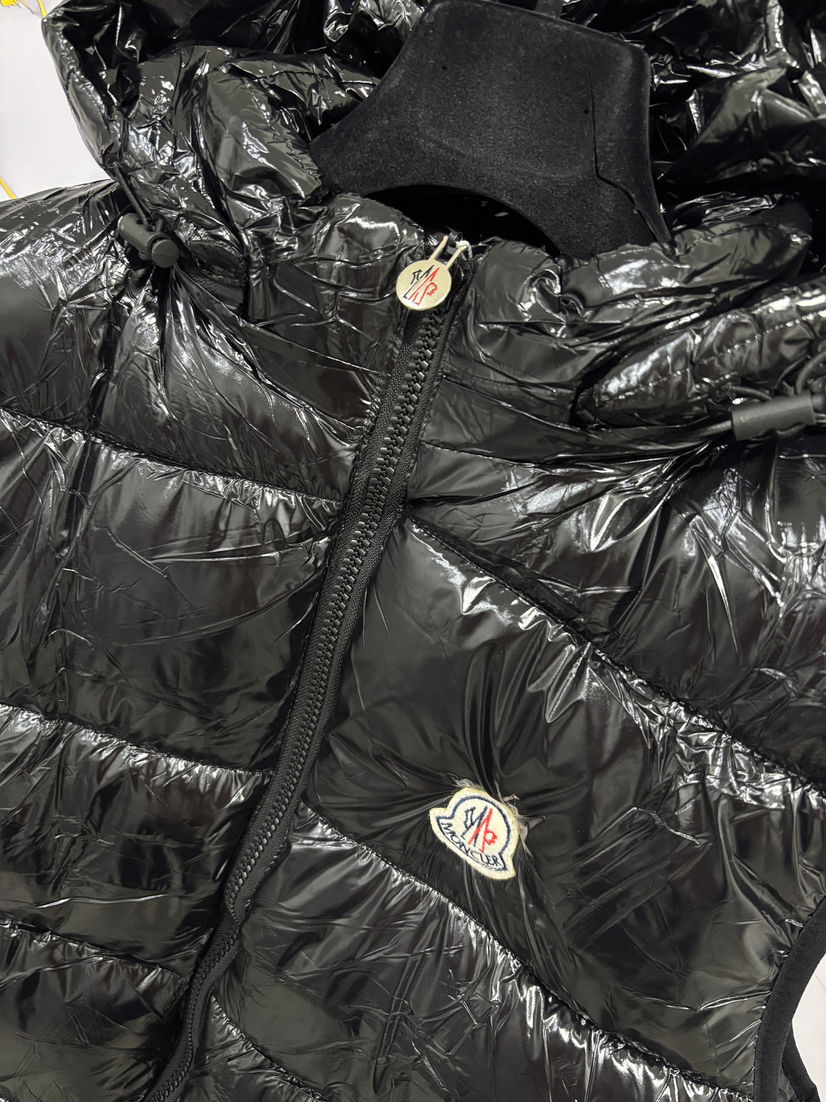 Close-up of SMANICATO MONCLER jacket with shiny black fabric and logo detail.